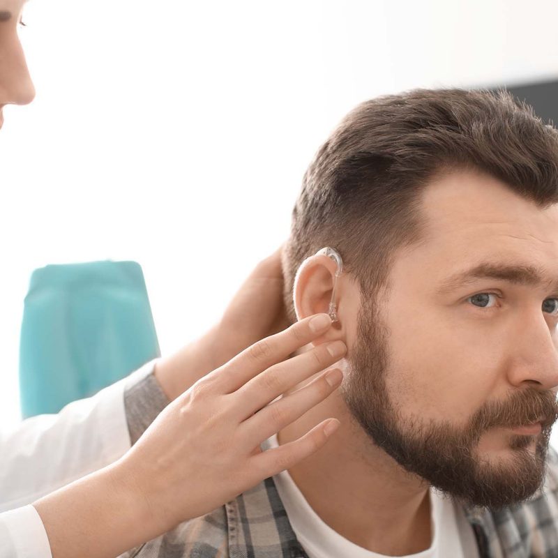 Otolaryngologist putting hearing aid in man's ear in hospital